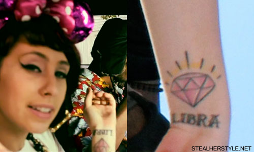 On Kreayshawn's left wrist are a pink diamond and the word Libra