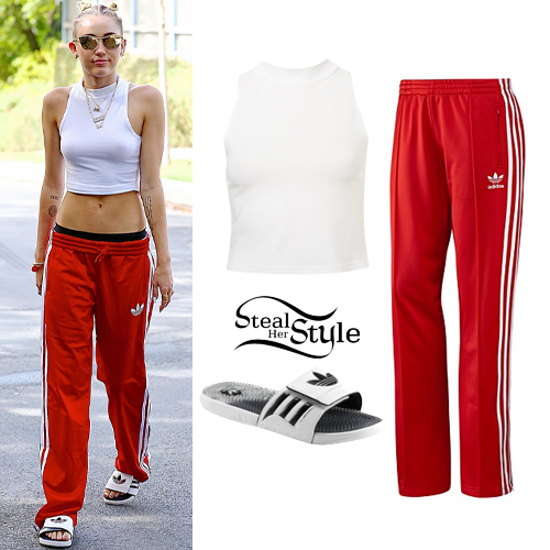 Miley Cyrus seen wearing a white tank top and Adidas track pants