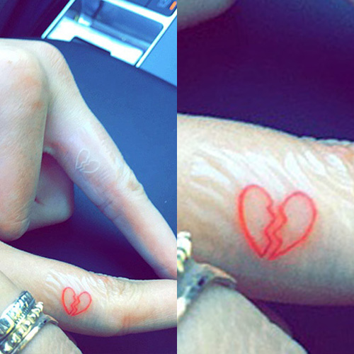 a tattoo featuring a small heart that is broken in half, inked in red on th...