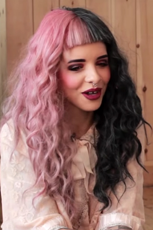 Melanie Martinez appears wearing curly pink and black hair while talking .....